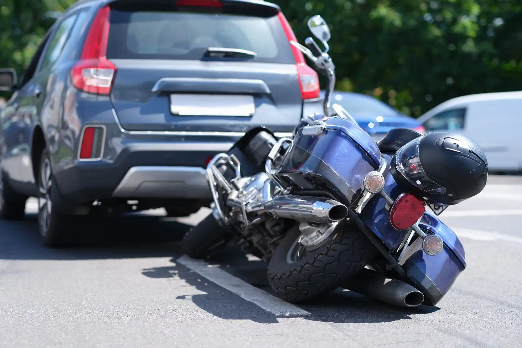 Motorcycle lying on its side on the road after colliding with the rear of an SUV, with a helmet resting on the seat.
