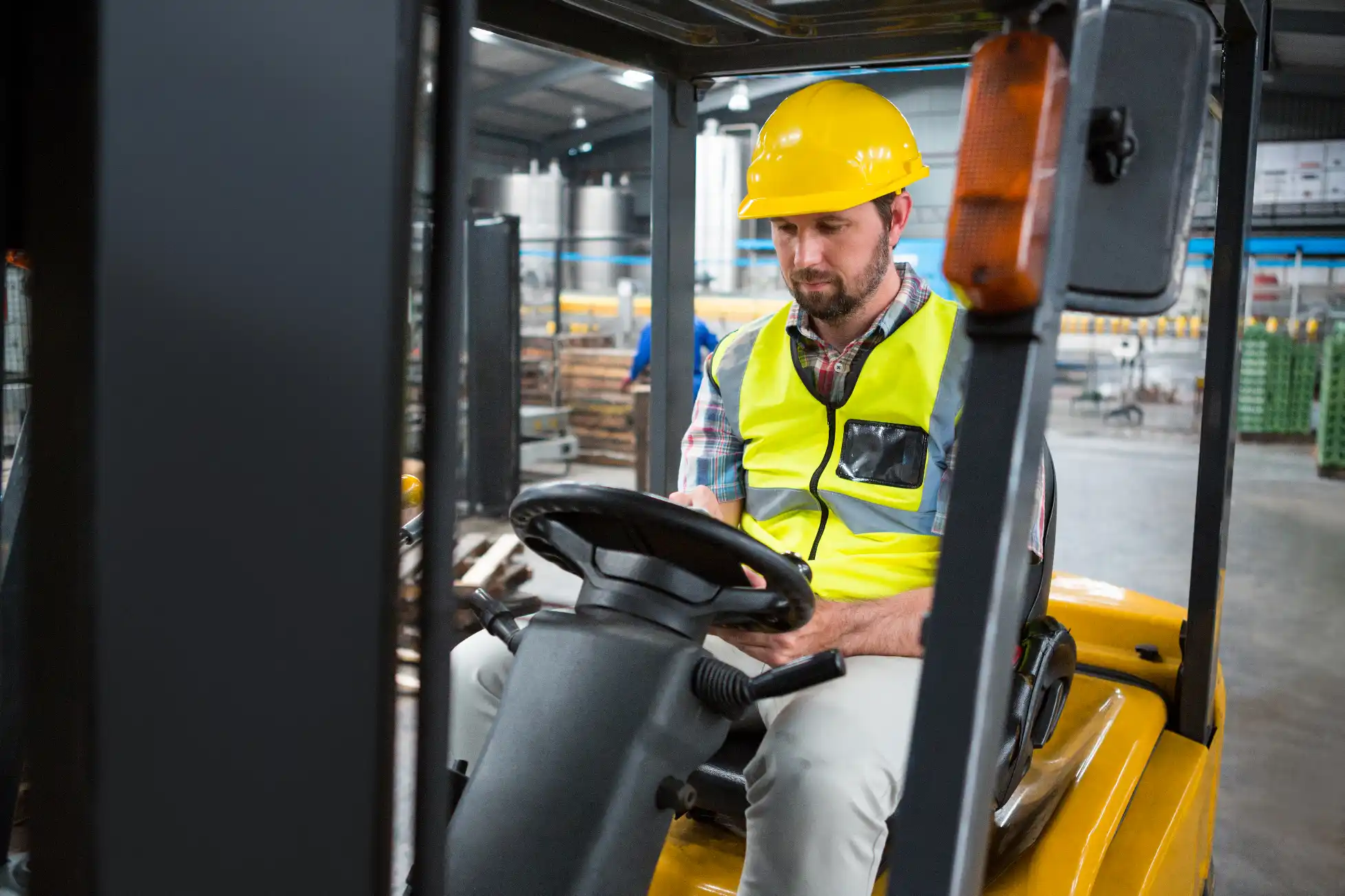A worker in a hi-vis vest and hard hat operating a yellow forklift inside a large industrial warehouse in Melbourne.